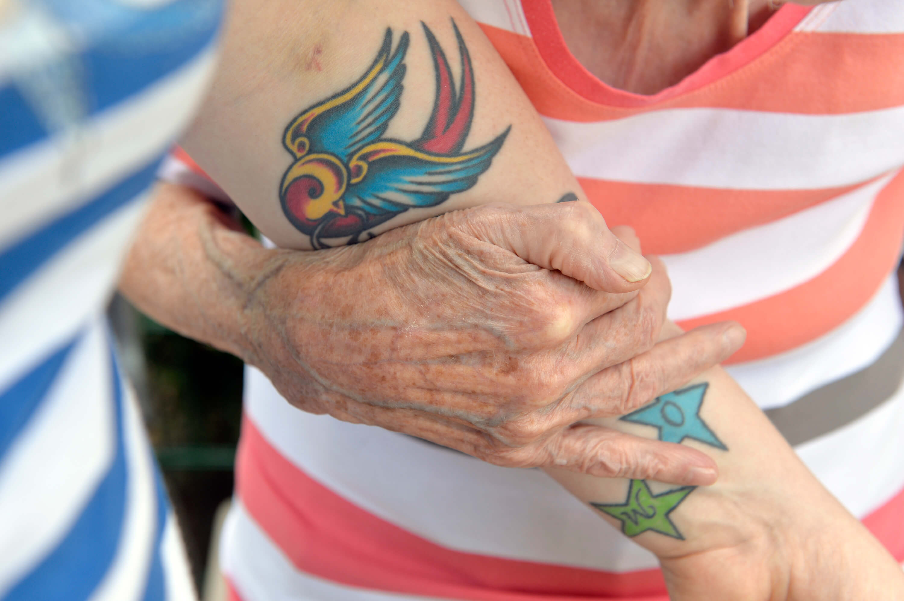 Hand eines alten Menschen, die an tätowiertem Arm untergehakt ist