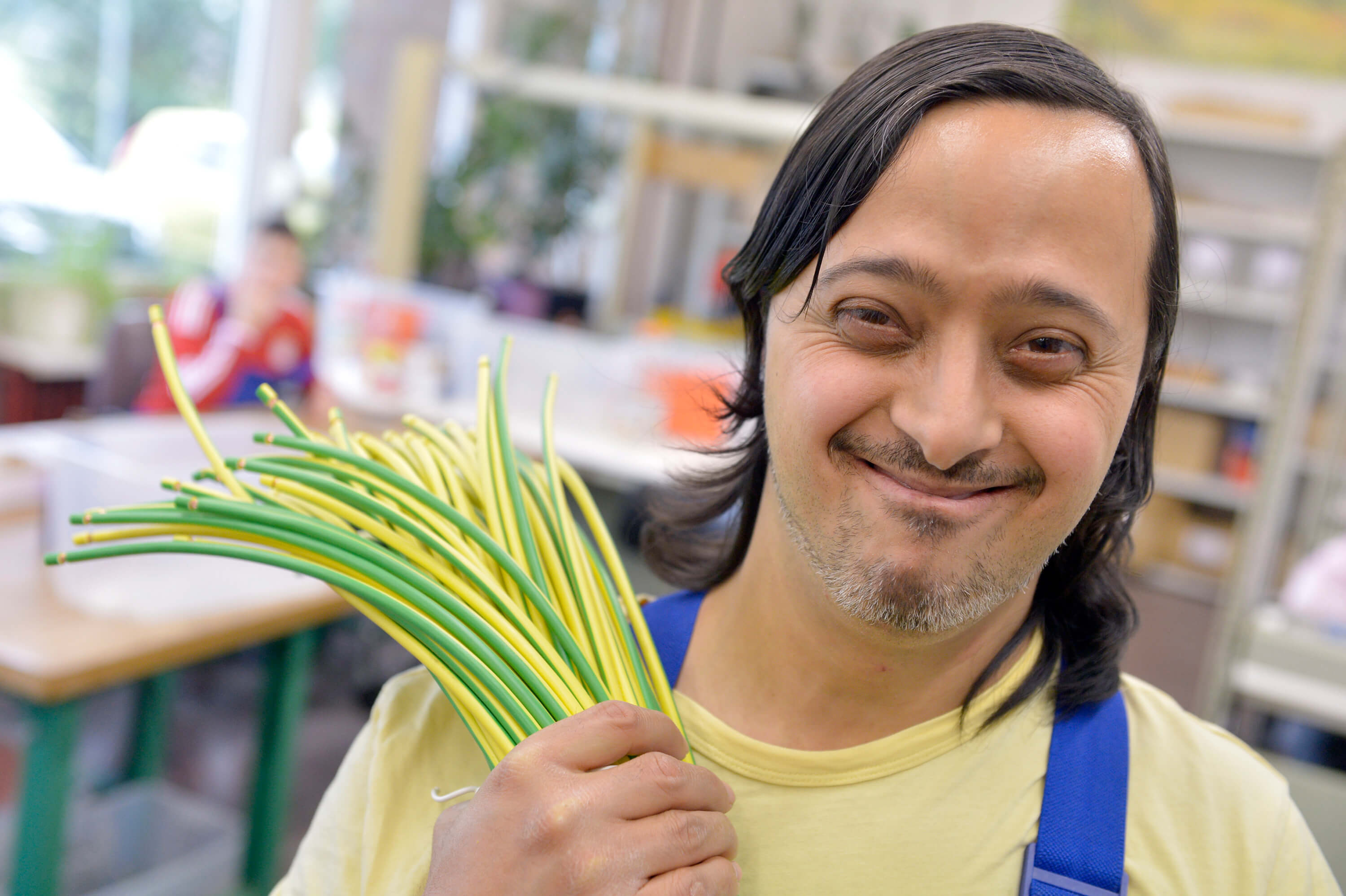 lachender junger Mann mit Down Syndrom bei der Arbeit, hält einen Bund Kabel in der Hand