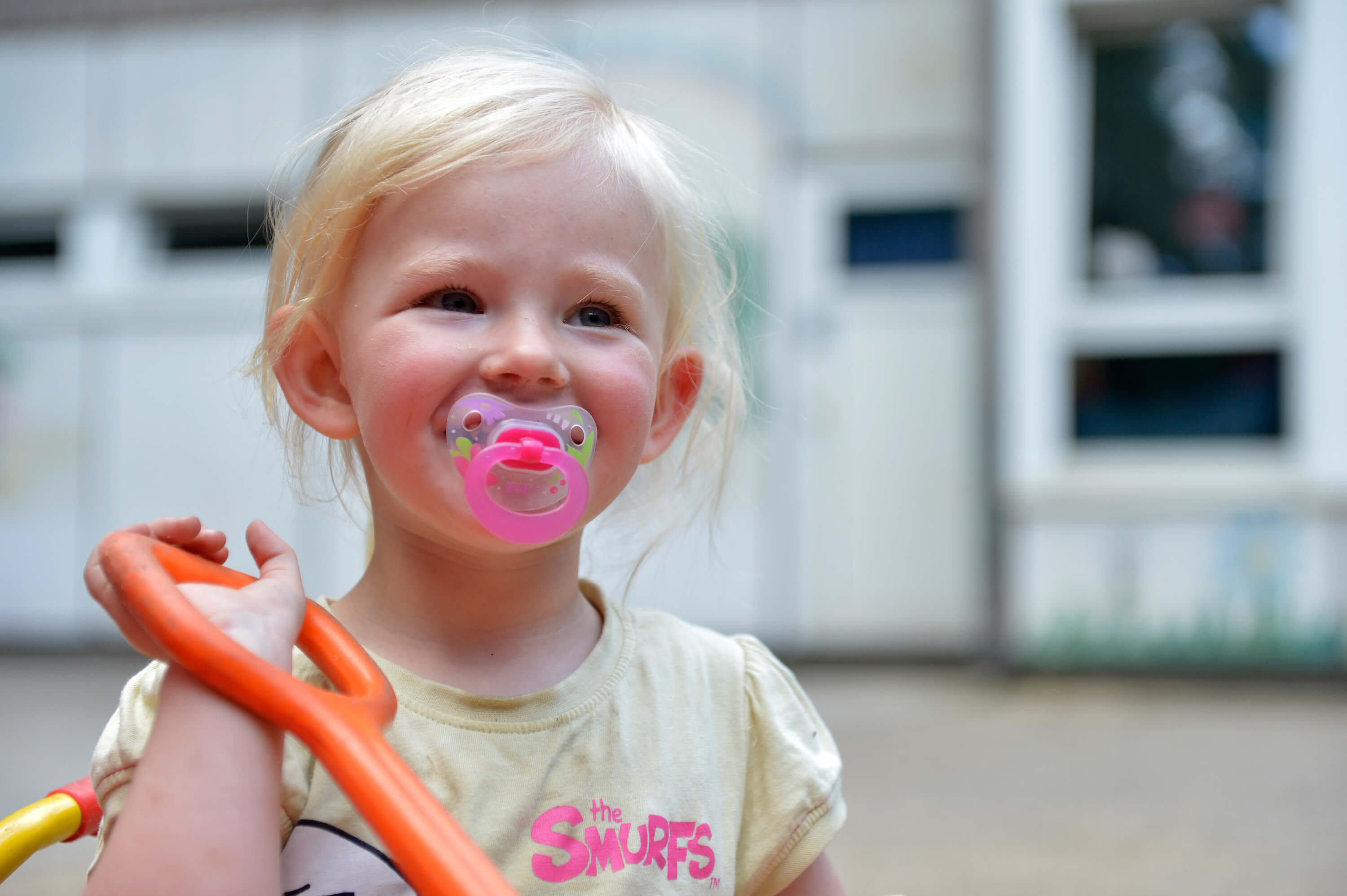 kleines lachendes Mädchen mit Schnuller, hält Schaufel in der Hand
